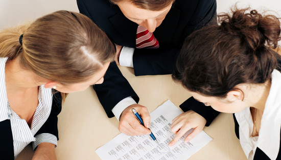 3 Personen sitzen an einem Tisch über eine ausgedruckte Tabelle gebeugt